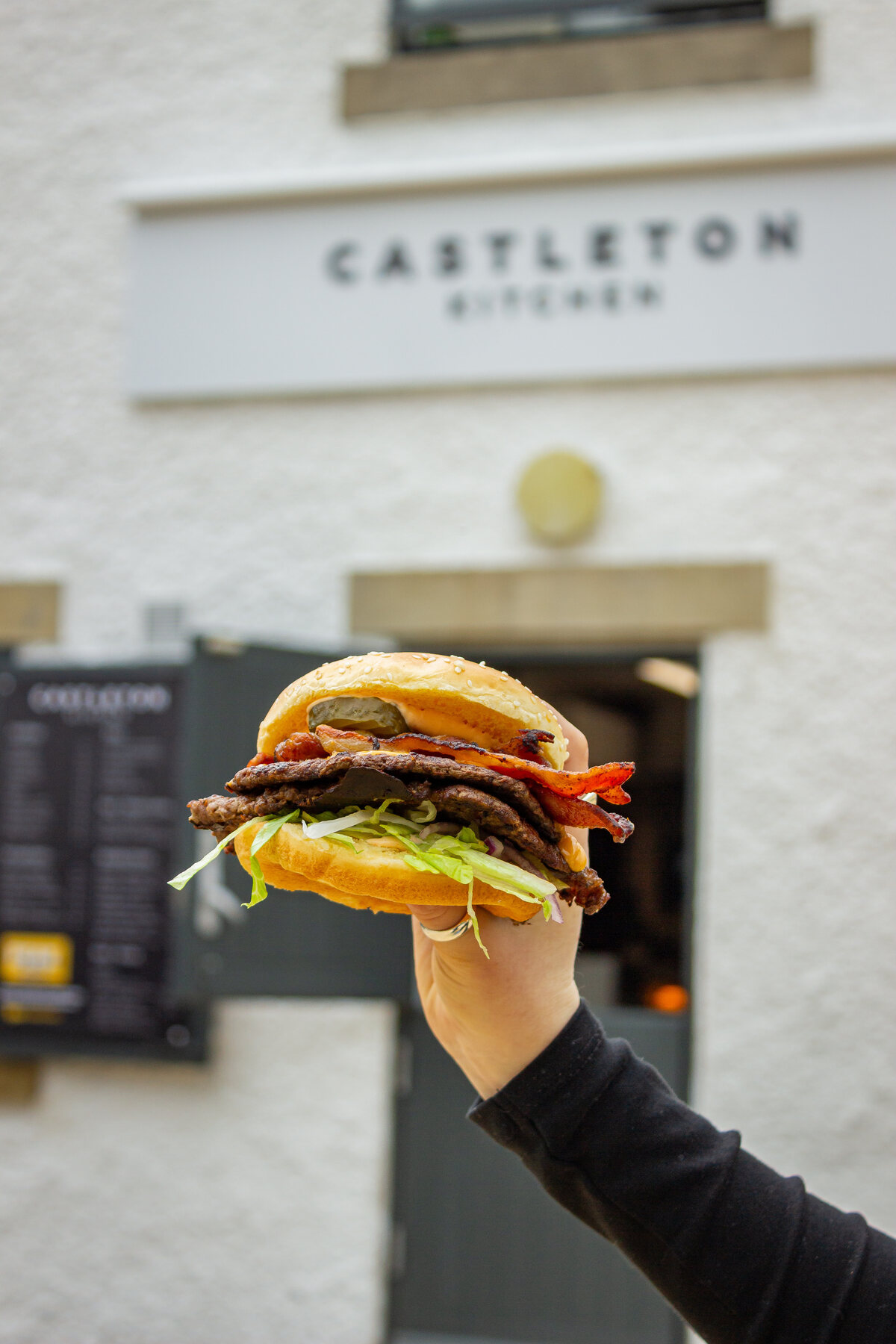A loaded Peak Burger Co smash burger held up outside Castleton Kitchen
